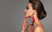 Profile of young woman wearing in a exquisite pink makeup with long brown hair gathered in a big elegant bun. Makeup, cosmetic and manicure.