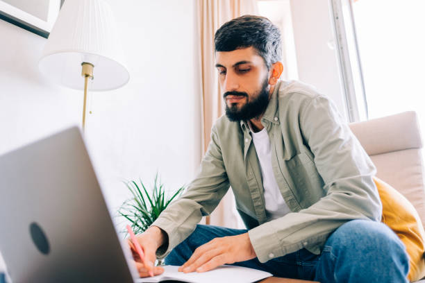 istock Caucasian man college student, studying with laptop distantly preparing for test exam writing essay doing homework at home, distantly education concept. 1339871878