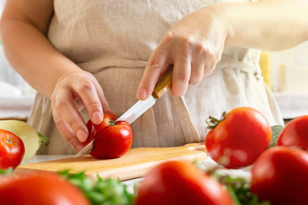 istock Chef slicing tomato using knife on the table in restaurant. Process of cutting and preparation food in kitchen. 1339874718
