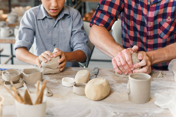 istock Cute caucasian boy making part of pots while his father kneading clay. 1339881985