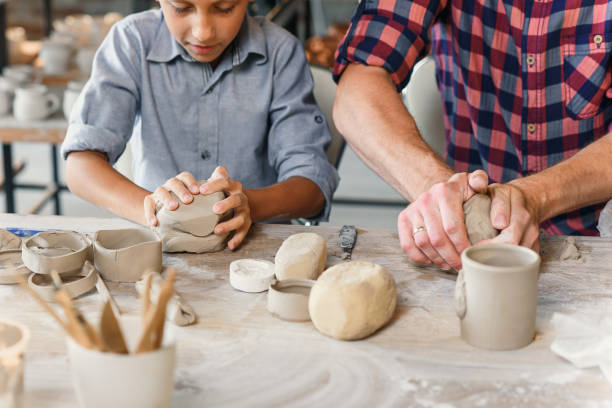 istock Cute caucasian boy making part of pots while his father kneading clay. 1339882204