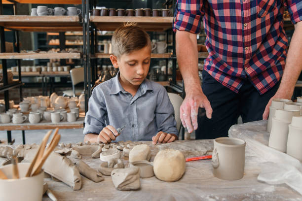 istock Middle aged caucasian man teaches his little brother to work with clay on pottery workshop. Art work concept. 1339882321
