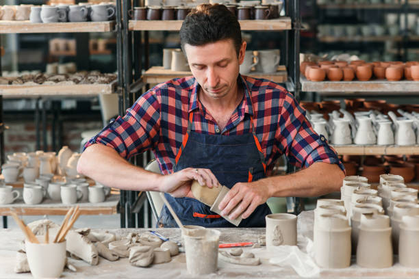 istock A middle-aged man in a work uniform wipes with a damp sponge a clay shape of cup in a large creative pottery workshop. 1339882447