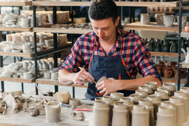 istock A middle-aged man in a work uniform make a clay shape of cup in a large creative pottery workshop. 1339883214
