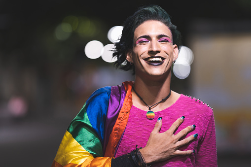 Smiling gay man with rainbow flag in the night city