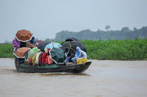Passengers traveling by wooden boat in the rain and protecting by umbrella.