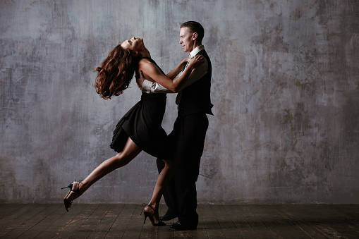 Couple dancers in black dress dancing tango against vintage grey background