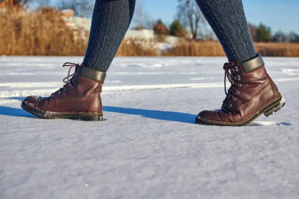 Photo of Female legs in leather brown waterproof boots is hiking in for winter on fresh snow. Casual fashion, trendy footwear.