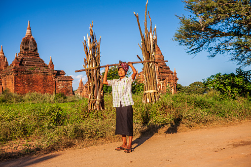 Portrait of burmese woman carrying brushwood on her head, Bagan, Myanmar.
