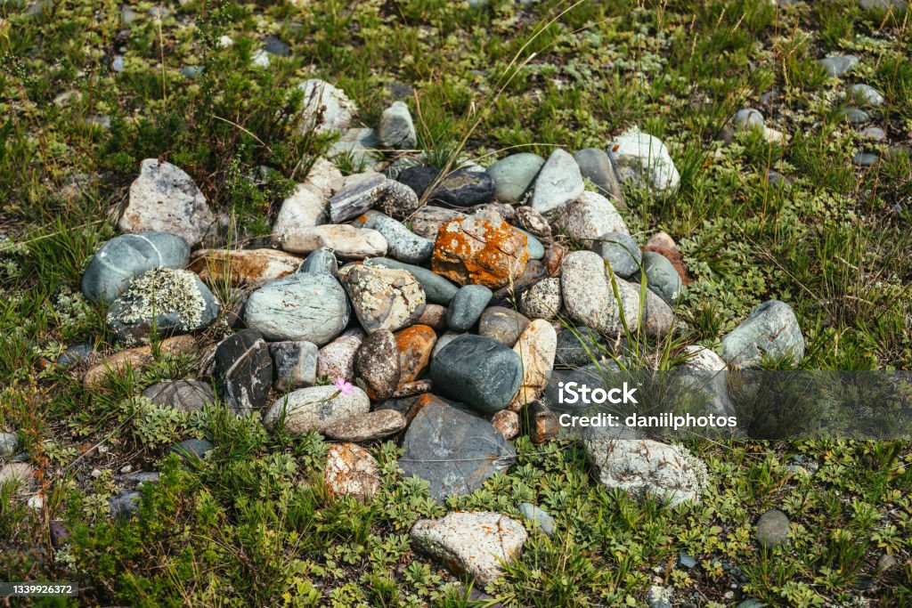 Pile of stones with lichen and moss on green grass. Art nature background with many stones on ground. Altai pagan cemetery. Ancient pagan burial place of Altaians. Pagan rite on Altai. Heap of stones. Altai Mountains Stock Photo