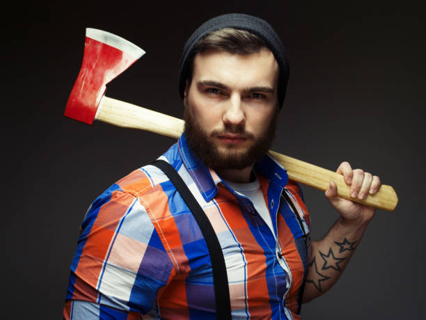 istock Bearded man wearing plaid shirt and balck hat with axe posing over black background in studio 1339929097