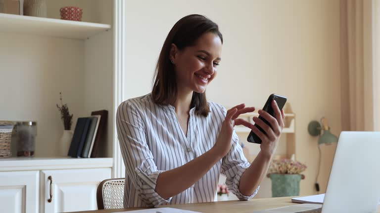 Young woman holding smartphone texting message seated at homeoffice