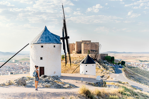Tourist standing on a hill with a group of restored antique windmills and a castle in Consuegra, Toledo in Spain