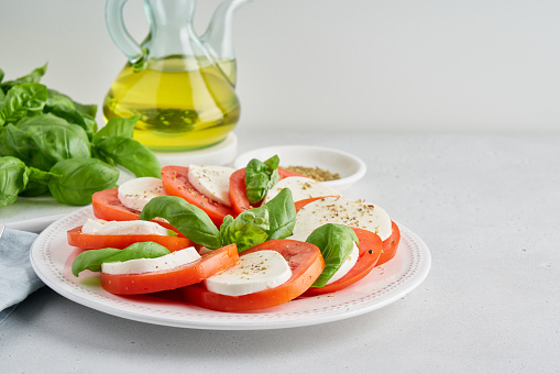 Horizontal of fresh italian caprese appetizer with mozzarella, tomatoes, basil, olive oil and spices on white background. Delicious vegetarian healthy salad. Side view, copy space