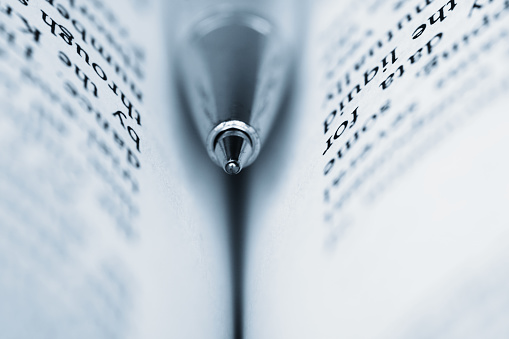 A blue ball pen embedded in an open book. Concept of education, study, research. Macro with shallow depth of field.