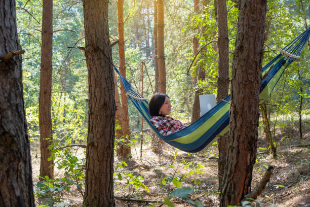 istock Freelance and IT. Freelancer woman works at notebook while lying on the hammock in the forest. Online business independent of the office. 1339966147