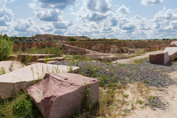 Large blocks of red granite with flat sides after stone cutting tool work and torn edges against the quarry and sky