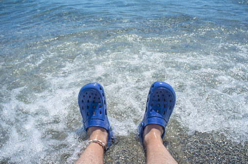 Male wearing blue clogs beside the beach. Selective focus