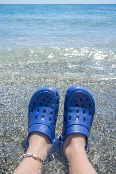 Male wearing blue clogs beside the beach. Selective focus