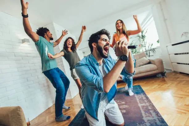 Photo of Group of friends playing karaoke at home.