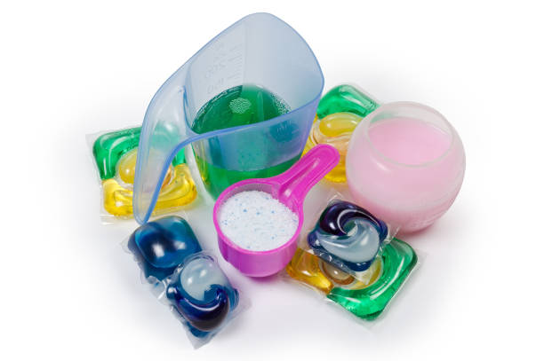 Powdered laundry detergent in measuring scoop, liquid detergent and washing gel in measuring cups and different laundry capsules on a white background