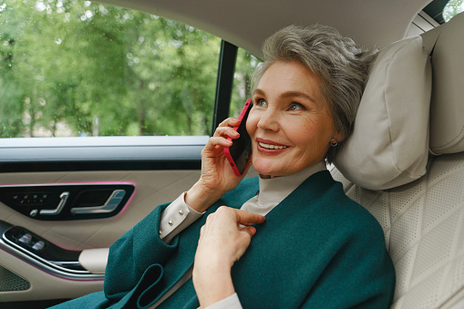 A beautiful businesswoman is cheerfully  talking on the phone on her way to the office, she is sitting on a backseat of the car with a white leather salon