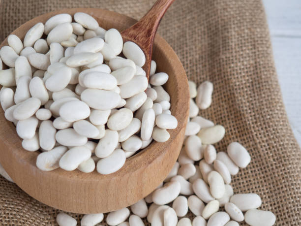 istock white beans in a wooden spoon on a white wooden table, copy space 1339976072