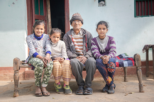 Indian village father sitting with his daughters on wooden cot outside his village house and smiling, happy family concept.