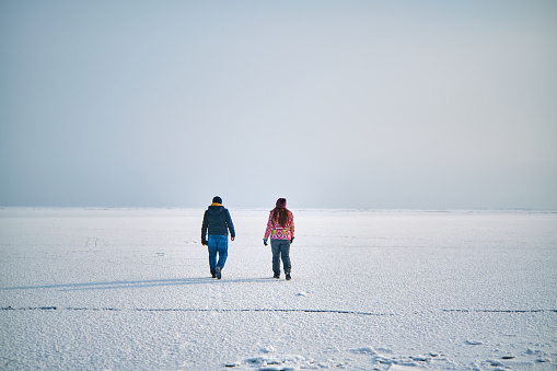 A guy and a girl are walking on a frozen lake, on ice, in winter