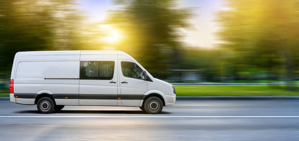 белый фургон передвигается по городской дороге на фоне закатного пейзажа. - van white truck mini van стоковые фото и изображения