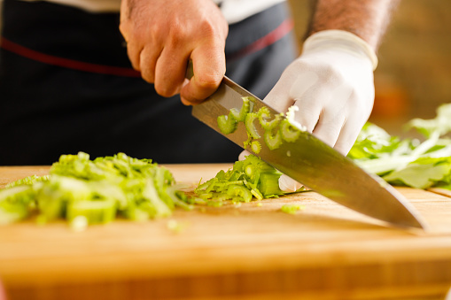 Close up of unrecognizable chef cutting celery with kitchen knife.