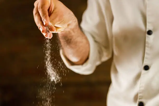 Close up of unrecognizable chef adding salt while preparing a meal in the kitchen.