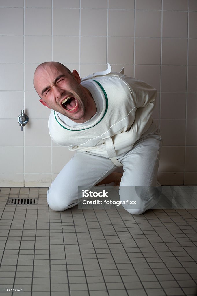 Chillar Psychopath en un corsé de hierro s'encuentra en un piso de baldosas - Foto de stock de Camisa de fuerza libre de derechos