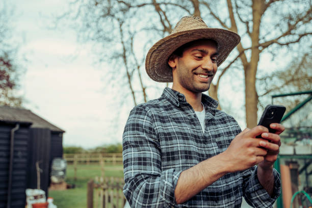 agricultor masculino mestiço mandando sms em dispositivo celular enquanto trabalhava ao ar livre - entrepreneur lifestyles nature environment - fotografias e filmes do acervo