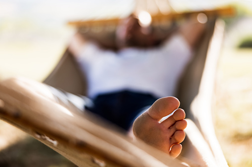 Close up of unrecognizable man's foot during relaxing time in hammock at the backyard.