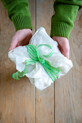 An unrecognisable man holding a tissue paper wrapped handmade present towards the camera. It is going to be given to someone as a Christmas gift.
