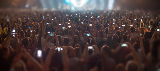 people at a concert are filming an artist's performance on a smartphone.