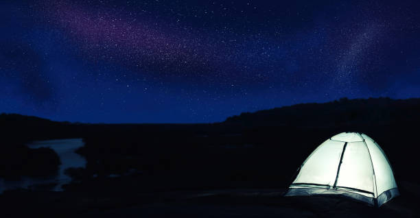 istock Modern camping tent glowing in twilight outdoors. Banner design 1339991297