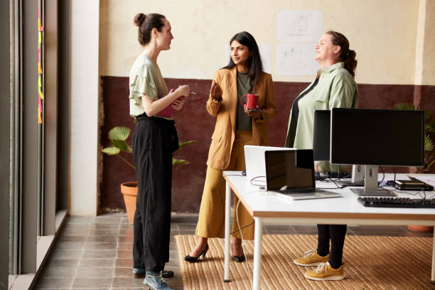 istock Three businesswomen standing next to a desk talking and drinking coffee. 1339993973