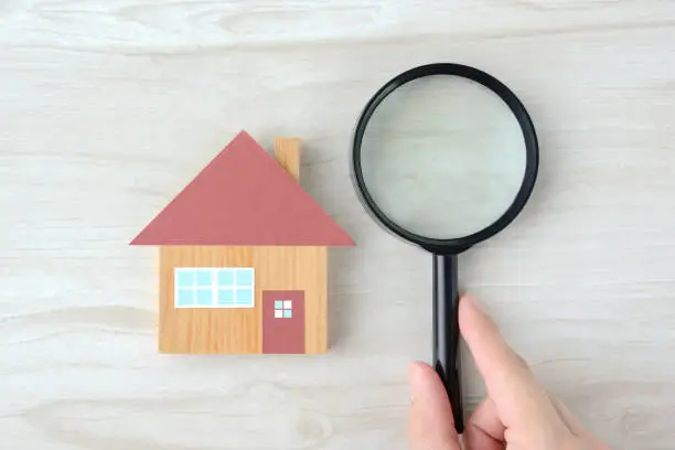 House object and human's hands with magnifying glass on natural wooden table