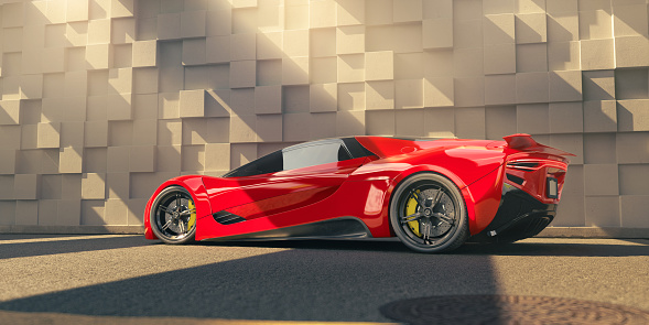 Low angle view of a generic red electric supercar parked at the side of a road next to a wall of organically protruding blocks in contemporary architectural style. The car is lit by sunlight coming in from above. With focus blur on the foreground.