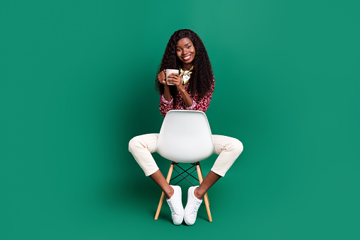 Photo of pretty sweet wavy dark skin lady wear print shirt sitting chair drinking coffee isolated green color background.