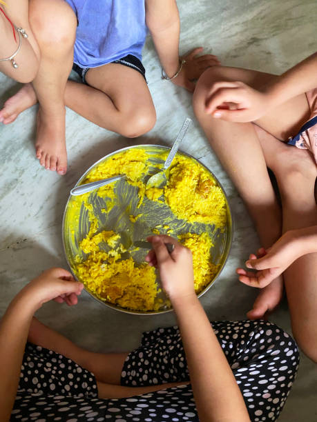 obraz grupy trójki nierozpoznawalnych indyjskich dzieci siedzących na podłodze wokół thali (metalowy talerz) jedząc sabji (mieszane warzywa) i ryż z metalowymi łyżkami, widok na wzniesieniu - children only healthy lifestyle vertical close up zdjęcia i obrazy z banku zdjęć