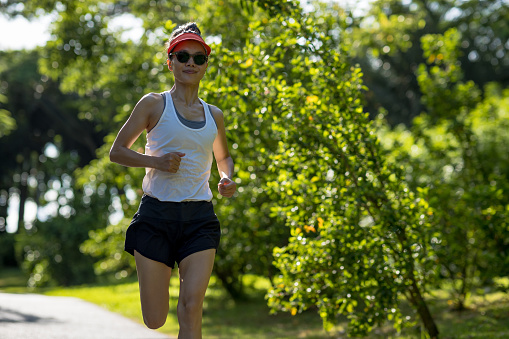 Fitness woman running on sunny tropical park trail