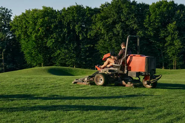 Photo of Greenkeeper. Golf course maintenance worker, cutting green grass