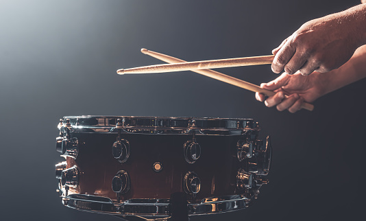 Snare drum and drummer's hands hitting drumsticks against a dark background.
