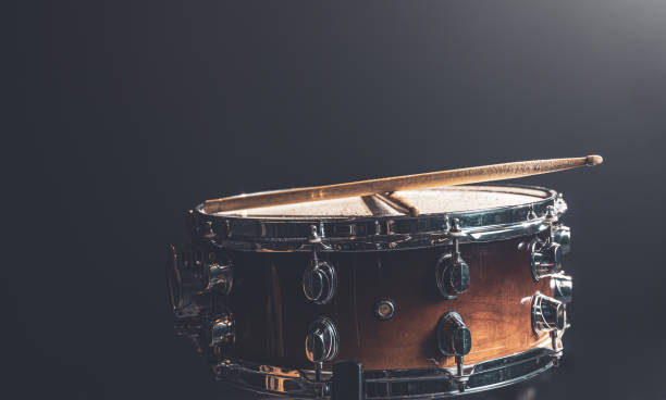 Close-up snare drum and drum sticks on a dark background. Close-up, snare drum, percussion instrument against a dark background with stage lighting. snare drum stock pictures, royalty-free photos & images