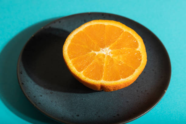 istock Ripe cut orange on blue ceramic plate on blue pastel background. Side view, close up, hard light. Tropical, healthy food, concept, minimalism. 1340013177