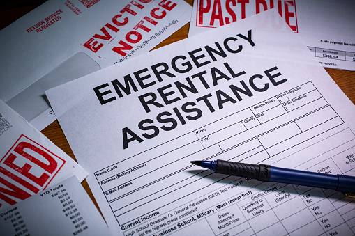 A blank application for Emergency Rental Assistance is on a desktop.  An Eviction notice and Past Due paperwork is nearby.