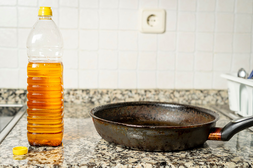Plastic bottle with recycled edible oil next to frying pan in the kitchen of a house. Recycling concept in the home